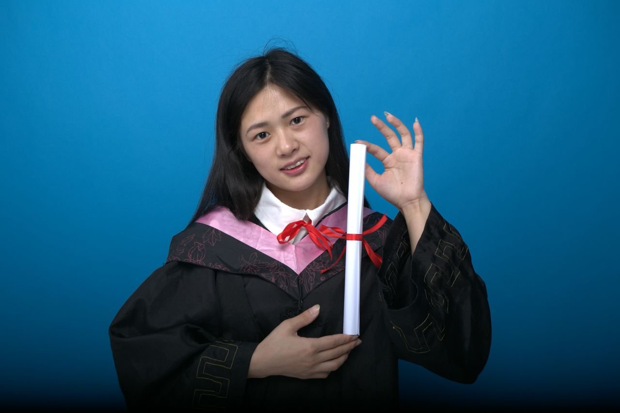 Study Abroad Asian female graduate holds diploma against blue background, smiling.