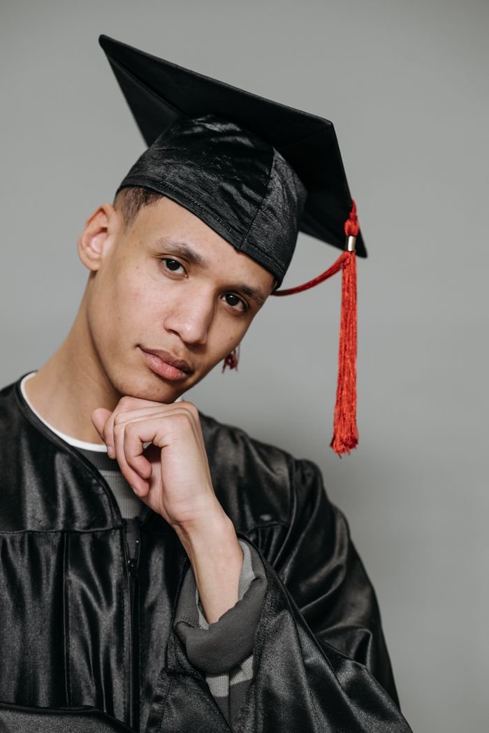 Study Abroad Pensive male graduate posing in a traditional cap and gown during a studio shoot.
