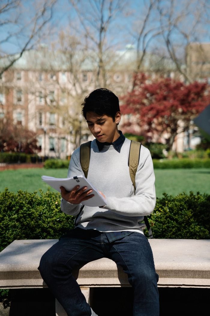 Study Abroad A young man sits on a concrete bench in a park, focused on studying outdoors.