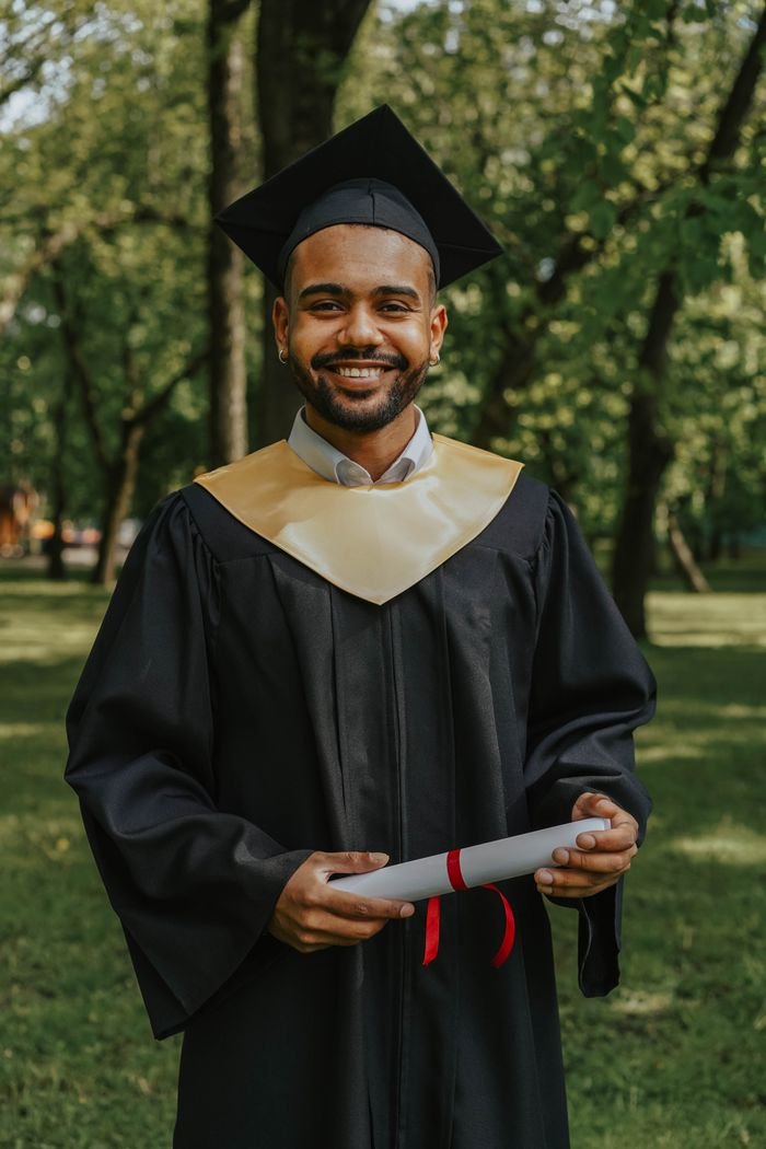 Home A joyful graduate in cap and gown holding a diploma in an outdoor setting.
