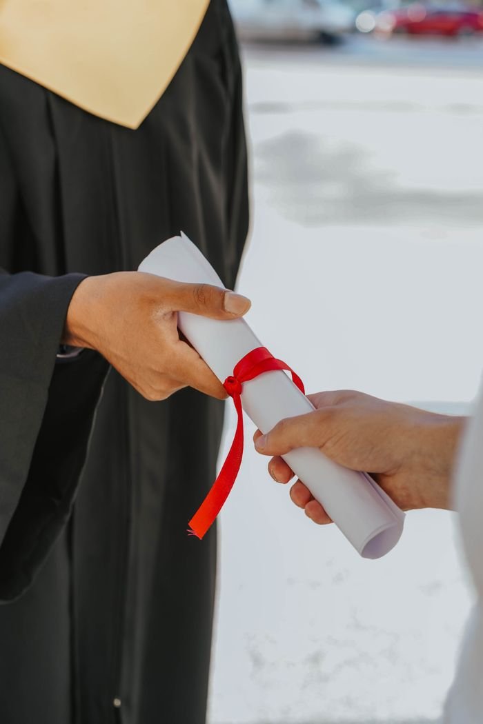 Study Abroad Hands exchanging a graduation diploma wrapped with red ribbon, symbolizing achievement.
