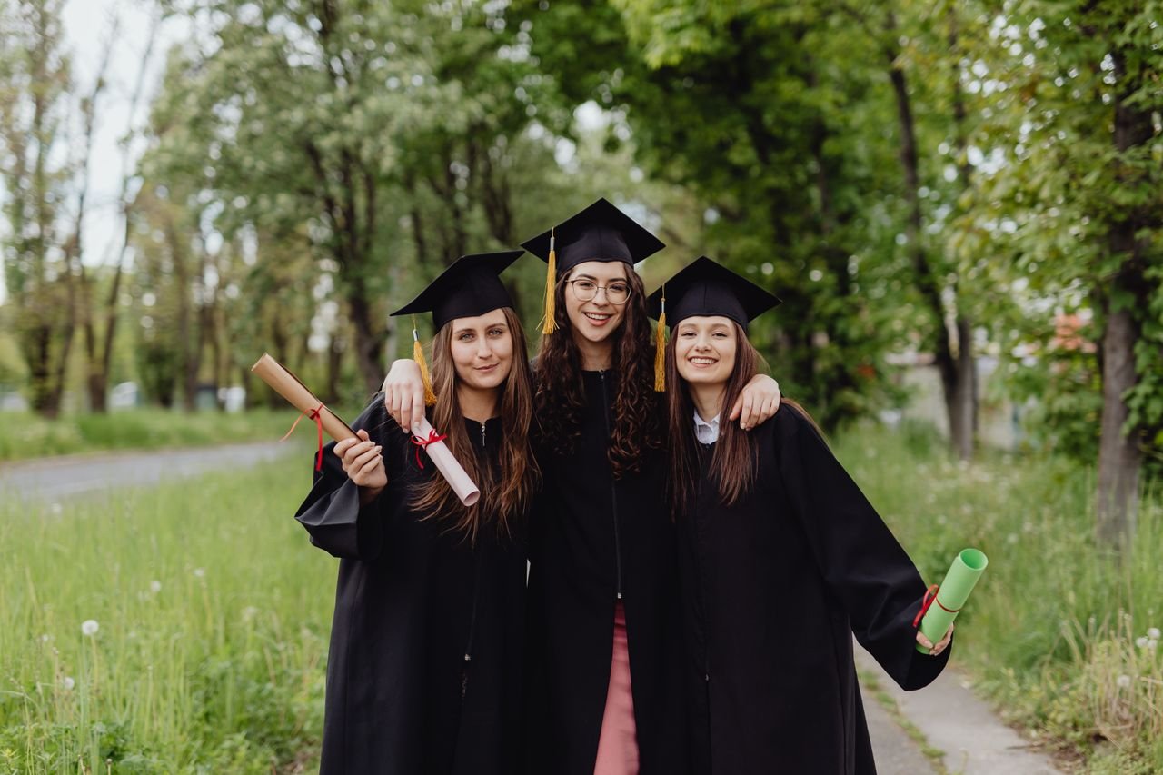 Study Abroad Three women in caps and gowns celebrate their graduation day outdoors.