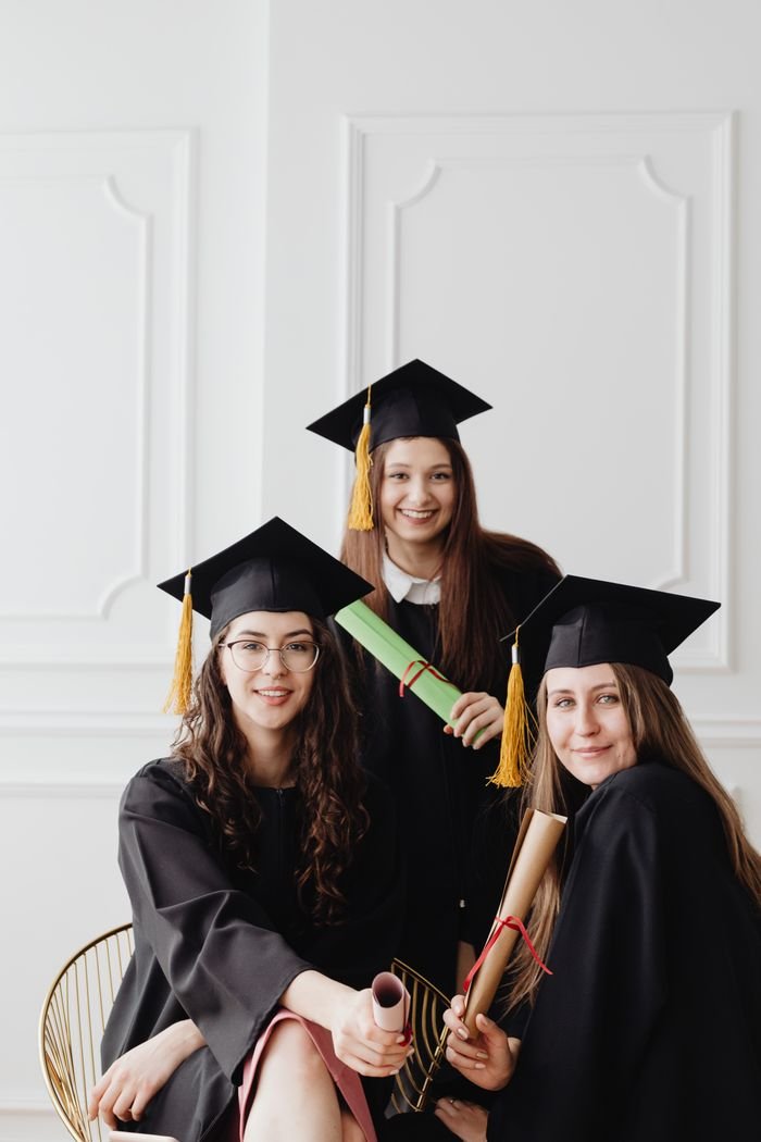 About Three female graduates in caps and gowns posing with diplomas indoors.